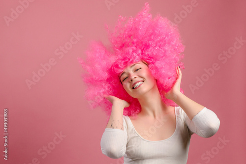 Smiling young pink haired woman dancing on pink background.