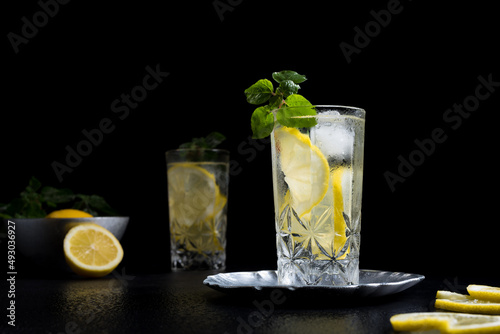 Un vaso de refrescante zumo de limón, cóctel de frutas con rodajas de limón y hielo sobre fondo negro