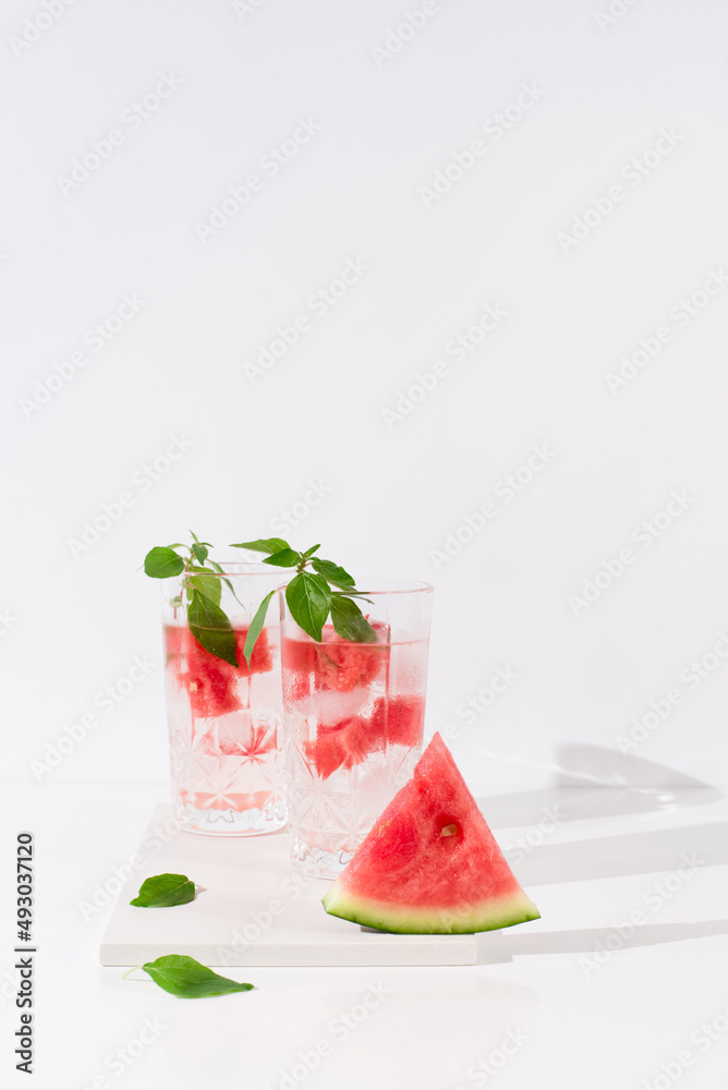 Dos vasos de zumo de sandía con trozos de sandia y hielo sobre fondo claro Dos vasos de zumo de sandía con trozos de sandia y hielo sobre fondo claro