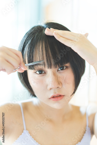 oung adult asian woman self cutting bangs haircut with scissors. Eyes looking at a camera