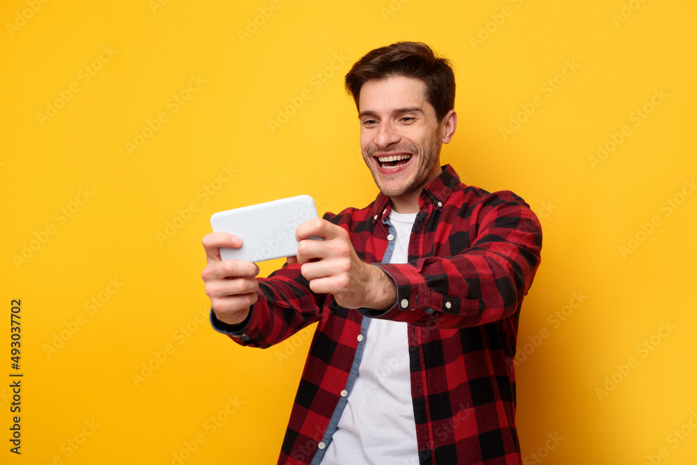 Excited man playing mobile games on yellow studio background Excited man playing mobile games on yellow studio background