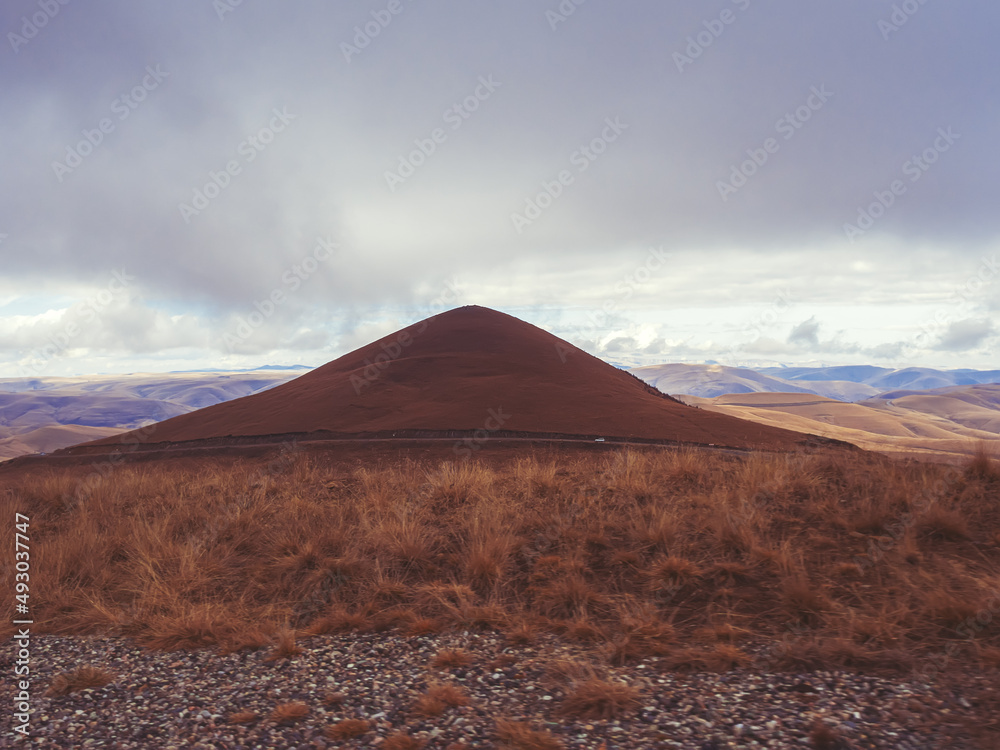 A mound in the form of a hill in a field with dry grass against the backdrop of a Caucasian mountain valley