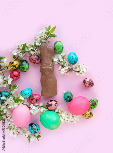 chocolate Easter bunny, colorful eggs and cherry flowers on pink background. symbol of Easter Christian holiday. spring festive decor. top view © Ju_see