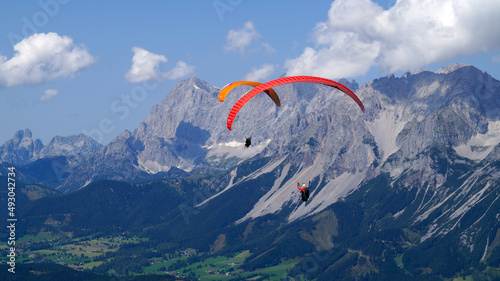 friends paragliding over the vast alpine valley surrounded by the scenic high Austrian Alps of the Schladming-Dachstein region (Austria)	