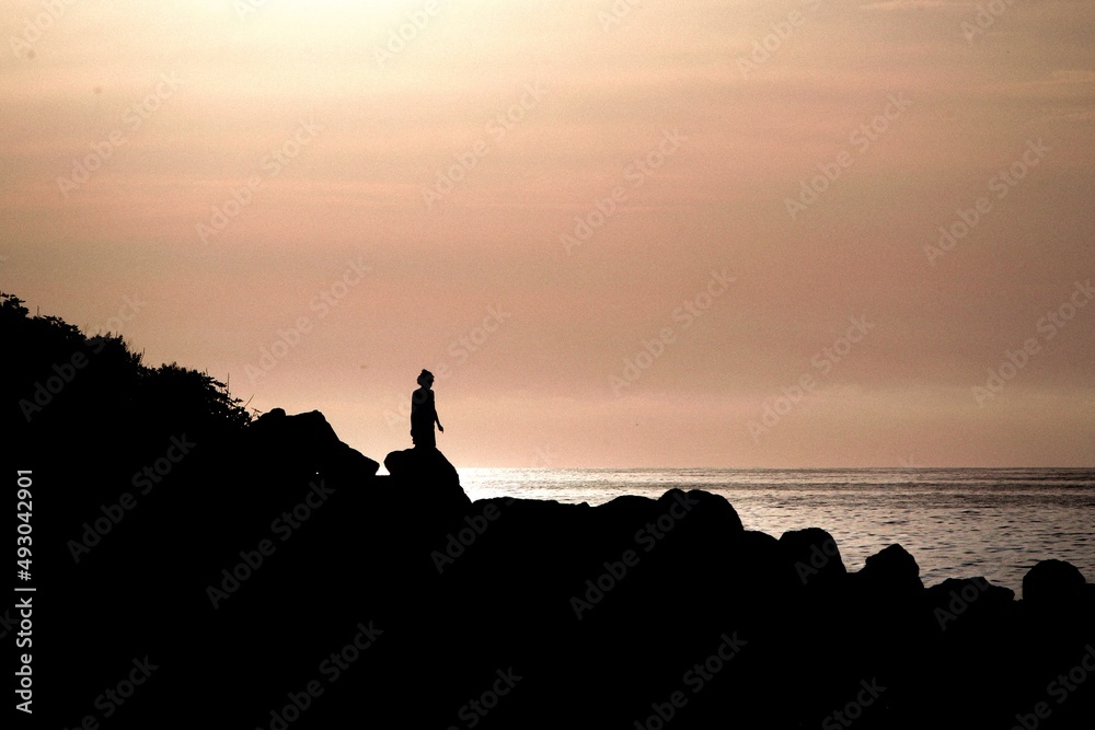 Silueta de niña pequeña juega a tirar piedras en un acantilado junto al mar