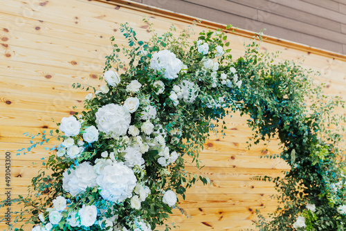 Close up of round arch decorated with white flowers and greenery for the wedding ceremony. Wooden background.