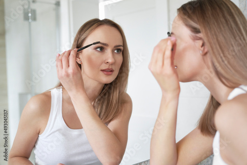 Young caucasian woman brushing eyebrows in the mirror reflection