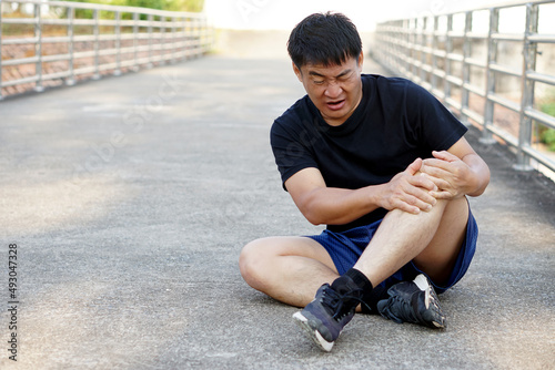 Asian Man runner gets hurt on his painful knee after running , jogging, exercise. Concept : injury knee twist sprain accident in workout or sport. Health problems. Copy space for text.