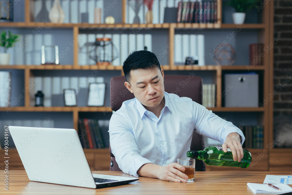 Asian businessman fails, man in despair drinks hard liquor, sitting late at the table in the office, depressed and hopeless Asian businessman fails, man in despair drinks hard liquor, sitting late at the table in the office, depressed and hopeless