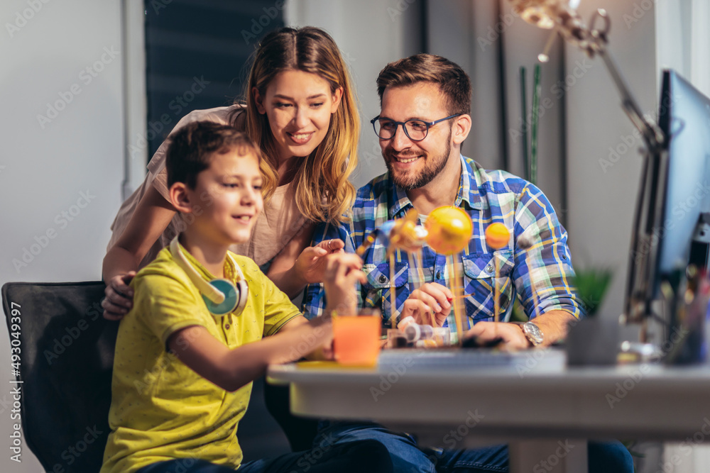 Obraz premium Happy school boy and his parent making a solar system for a school science project at home