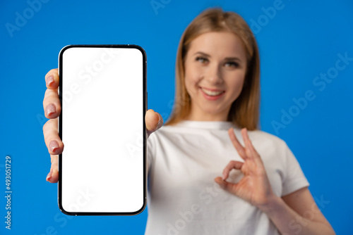 Young woman point finger at isolated smartphone screen over blue color background