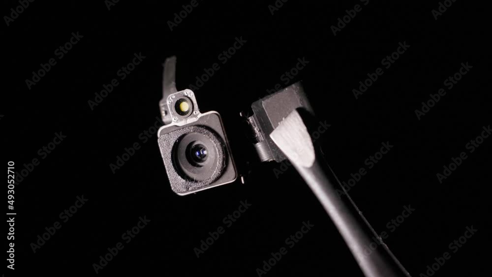 A close-up camera module appears from the darkness and disappears. Hidden camera on black background A close-up camera module appears from the darkness and disappears. Hidden camera on black background
