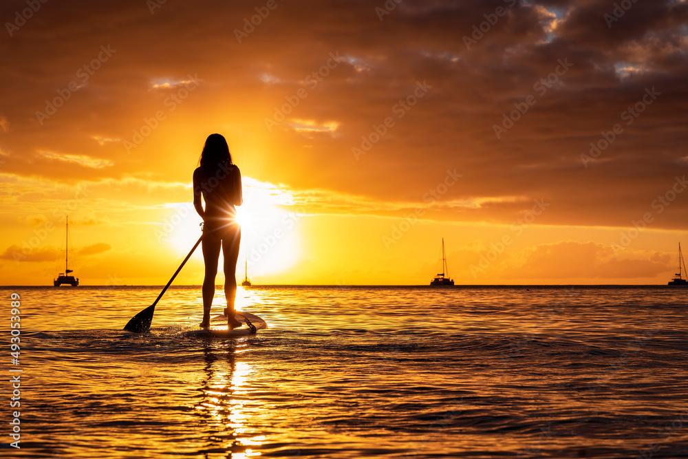 Silhouette of a woman on a stand up paddle board (SUP) on calm sea during golden sunset time