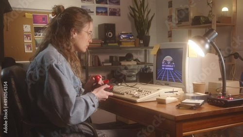 A teenager girl playing with a 90s retro game in a personal computer in her bedroom. photo