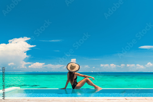 Luxury summer vacation tourist woman relaxing by swimming pool. Elegant lady relaxing sunbathing enjoying travel holidays at resort infinity overwater pool. Luxury lifestyle. © Maridav