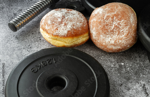 Dumbbells barbell weight plates and Polish pączki deep-fried doughnuts. Fat Thursday (Tłusty czwartek). Pączek, traditional feast day in Poland. Fitness gym workout, cheat day vs sticking to diet. photo