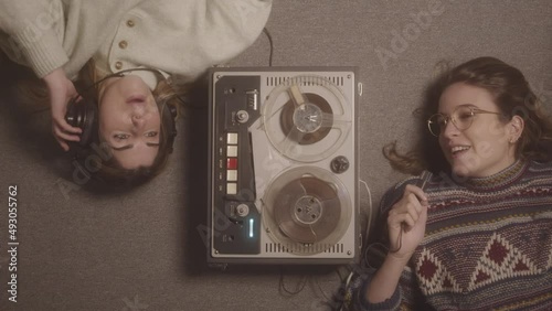 Couple of girls lying on a rug singing and humming their favorite song on an old tape recorder