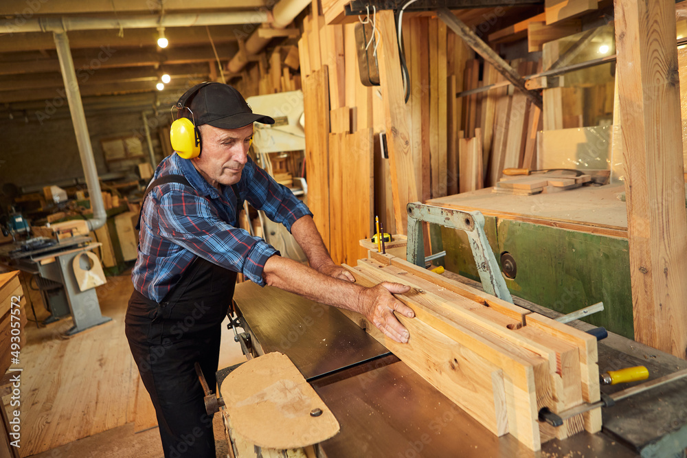 Senior carpenter in uniform works on a woodworking machine at the carpentry manufacturing Senior carpenter in uniform works on a woodworking machine at the carpentry manufacturing