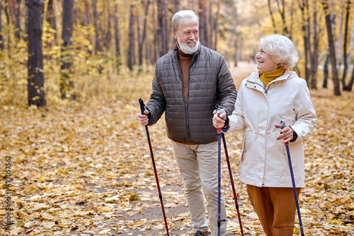 Foto Happy aged couple in love engaged in Nordic walking going in autumn nature park, forest