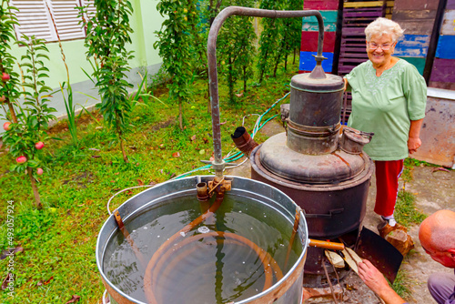 Woman is manually mixing fruit marc in distillation apparatus for making domestic alcohol liquor photo