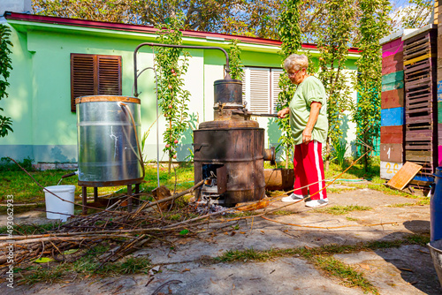 Woman is manually mixing fruit marc in distillation apparatus for making domestic alcohol liquor