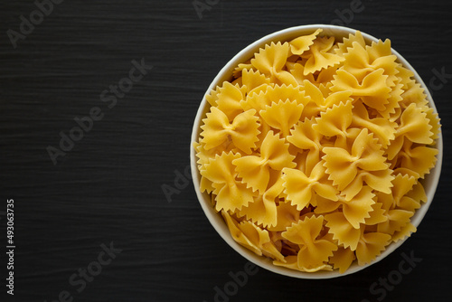 Raw Organic Farfalle Pasta in a Bowl on a black background, top view. Flat lay, overhead, from above. Space for text.