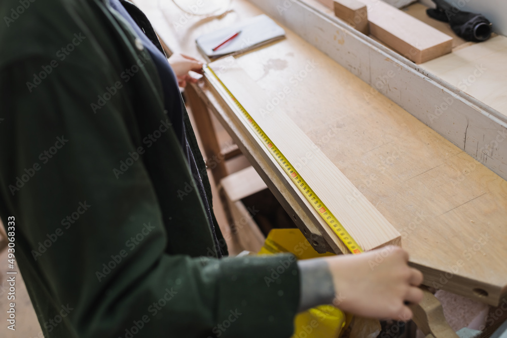 Cropped view of carpenter holding tape measure near wooden board in workshop. Cropped view of carpenter holding tape measure near wooden board in workshop.