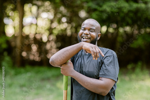 Black farmer smiles and leans on the handle of a farm tool photo