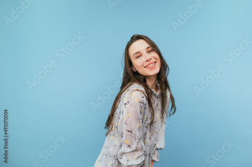 Attractive woman in dress with smile on face posing at camera on blue background. © bodnarphoto