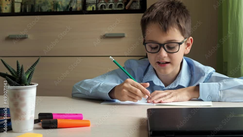 a teenager in a blue shirt talks to the camera after continuing to write in a notebook. sitting at a desk. for lessons a teenager in a blue shirt talks to the camera after continuing to write in a notebook. sitting at a desk. for lessons