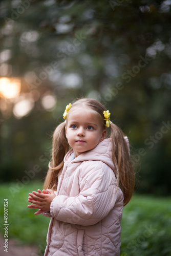 Small blonde european girl portrait with pig-tails with flowers in evening, outdoors, in forest. Big eyes and smart smile