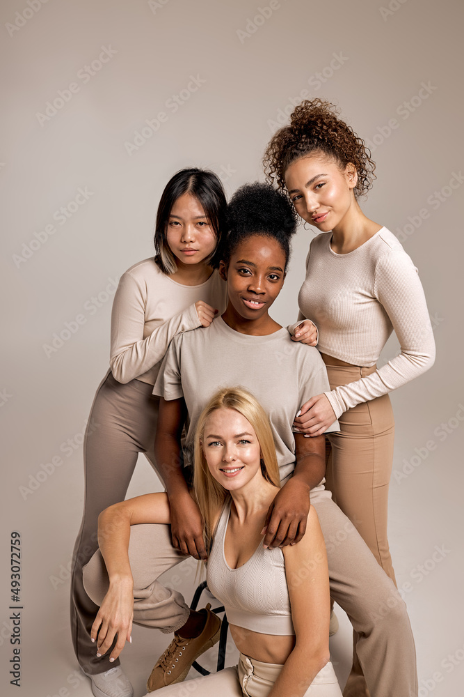 Positive smiling women with diverse appearance and natural make-up posing together, attractive ladies in casual clothes look at camera having cute smile on face, isolated on beige background Positive smiling women with diverse appearance and natural make-up posing together, attractive ladies in casual clothes look at camera having cute smile on face, isolated on beige background