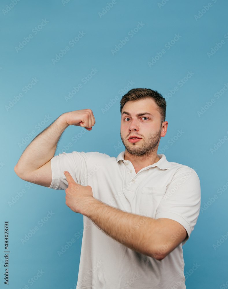 A strong man in a white T-shirt and with bristles brags his biceps to the camera and looks with a serious face. Vertical. A strong man in a white T-shirt and with bristles brags his biceps to the camera and looks with a serious face. Vertical.