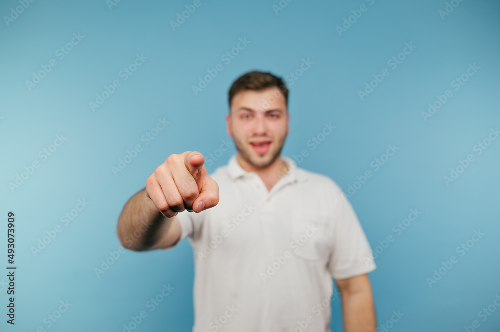 Positive man in white t-shirt pointing finger at camera and smiling, isolated on blue background Positive man in white t-shirt pointing finger at camera and smiling, isolated on blue background