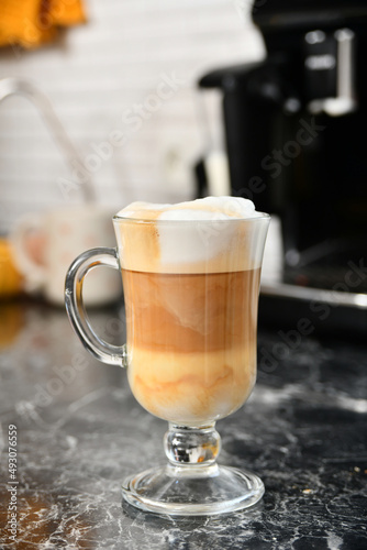 A glass cup with espresso coffee with milk is on the table.