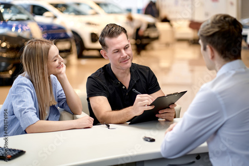 caucasian married couple with dealer buying car and signing documents, having talk with manager in auto show or salon. automobile, vehicle, transport, sales, people concept