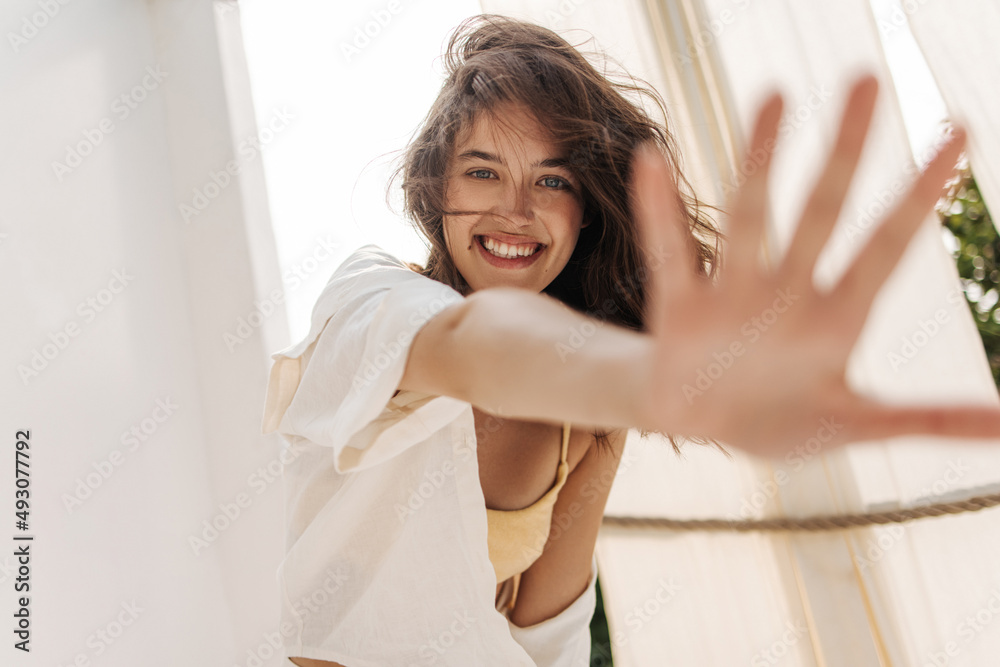 Beautiful fair-skinned young lady with tousled dark hair reaches for camera outdoors. Girl with snow-white smile in white clothes. People sincere emotions lifestyle concept. Beautiful fair-skinned young lady with tousled dark hair reaches for camera outdoors. Girl with snow-white smile in white clothes. People sincere emotions lifestyle concept.