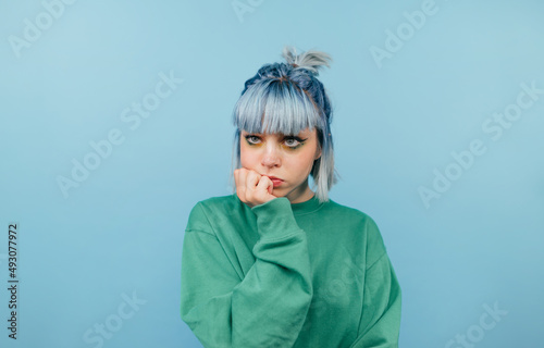 Pensive casual girl with blue hair isolated on blue background, looks away and thinks