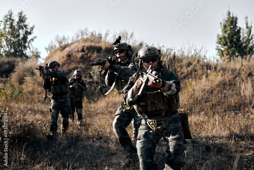 Fully Equipped Soldiers Wearing Camouflage Uniform Going To Attack Enemy, Rifles Weapons in Firing Position. Military Operation in Action, Squad Running in Mountains Field In Nature.