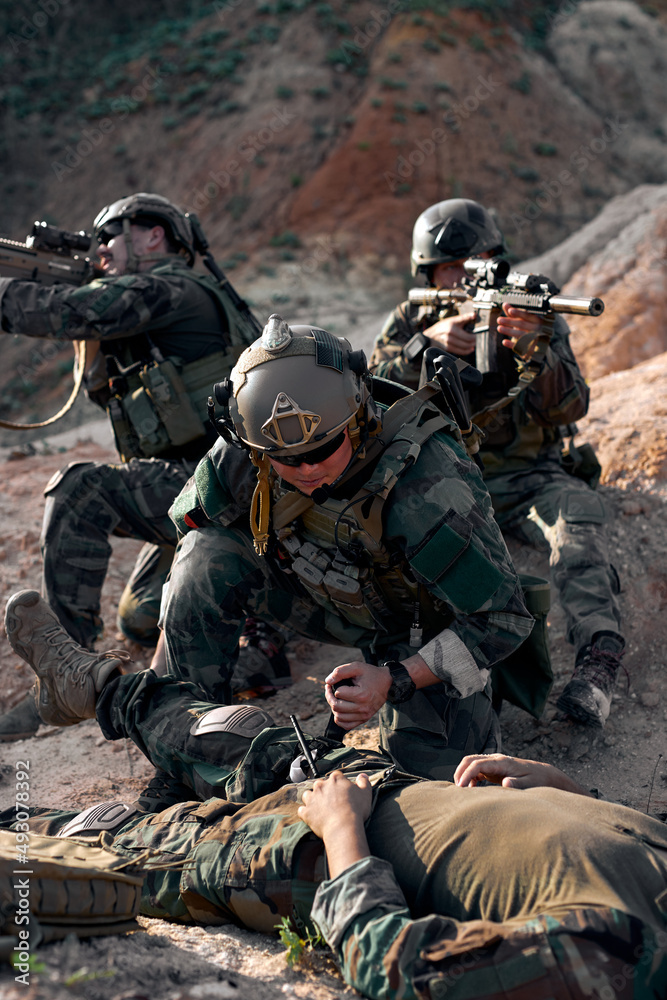 soldier saving life of injured comrade lying on ground, need medical help. outdoors in mountains. Private Military Contractor during the rescue operation. counter terrorism concept. soldier saving life of injured comrade lying on ground, need medical help. outdoors in mountains. Private Military Contractor during the rescue operation. counter terrorism concept.