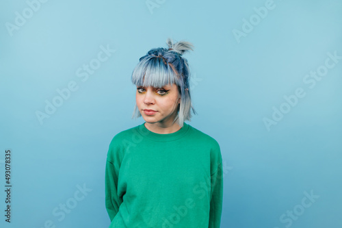 Foto Beautiful hipster girl in a green sweater and with blue hair isolated on a blue background looking at the camera with a serious face