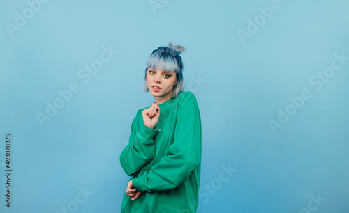 Informal positive girl in a green sweater and blue hair with a smile on her face posing for the camera. Isolated on blue background