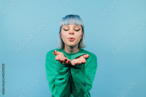 Cute lady with blue hair sends air kisses to the camera on a blue background.