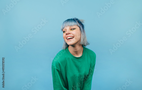 Attractive lady with colored hair with a smile on her face isolated on a blue background in a green sweater looking aside