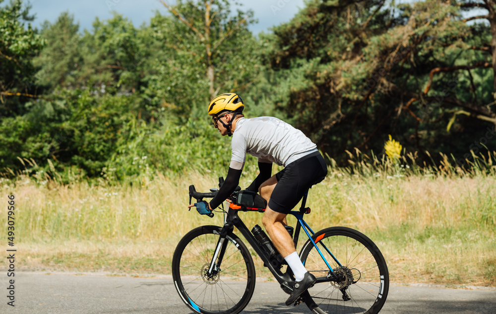 Photo of a man in sports outfit rides a bike on a forest road on a sunny day, side view.