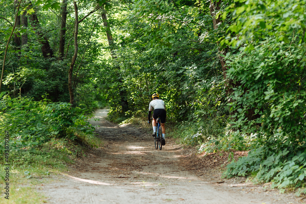 Fototapeta premium Cyclist rides on a dirt road on a bicycle, view from the back.