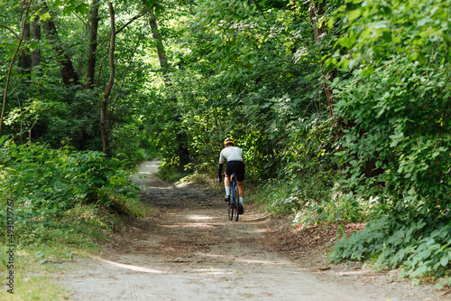 Cyclist rides on a dirt road on a bicycle, view from the back. © bodnarphoto
