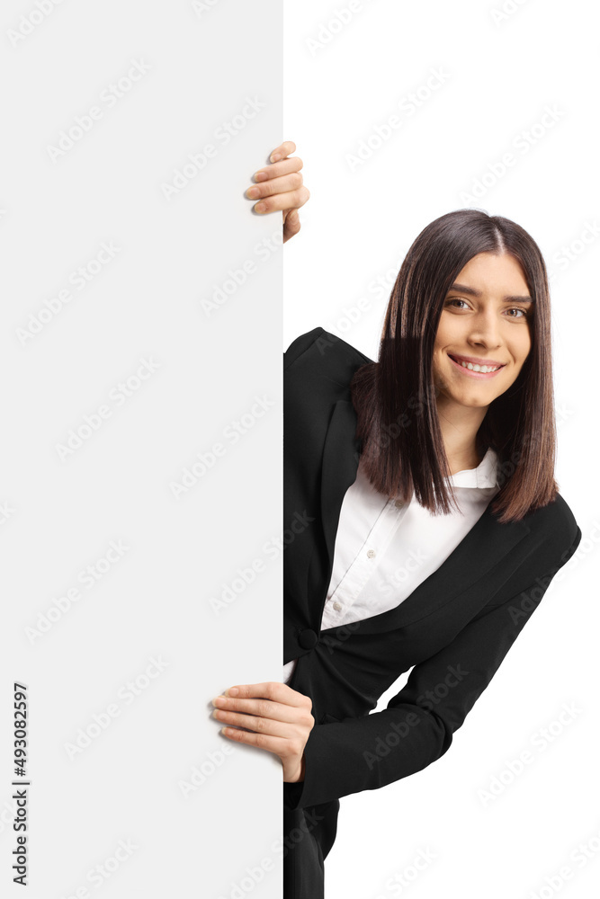 Young woman in formal clothes peeking from behind a blank white panel Young woman in formal clothes peeking from behind a blank white panel