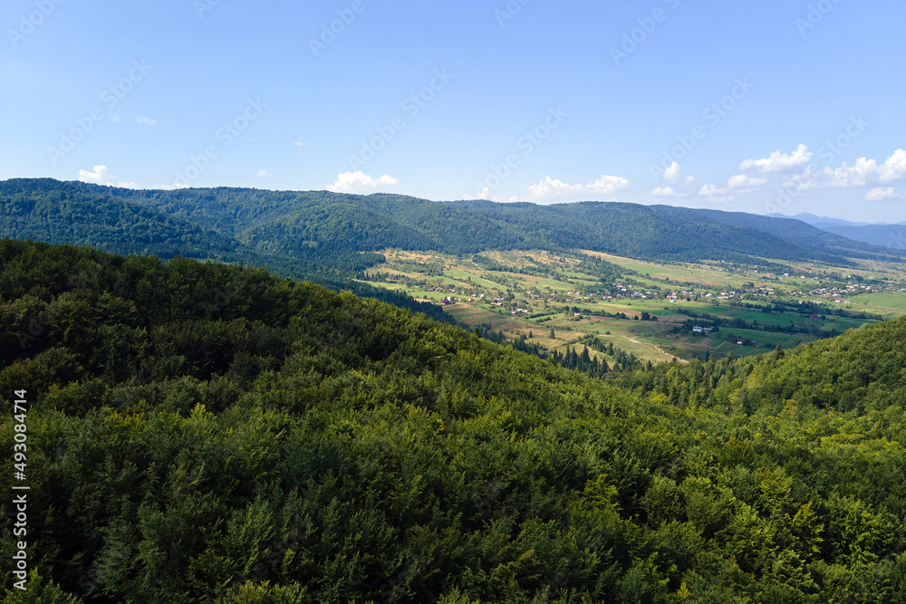 Aerial view of mountain hills covered with dense green lush woods on bright summer day