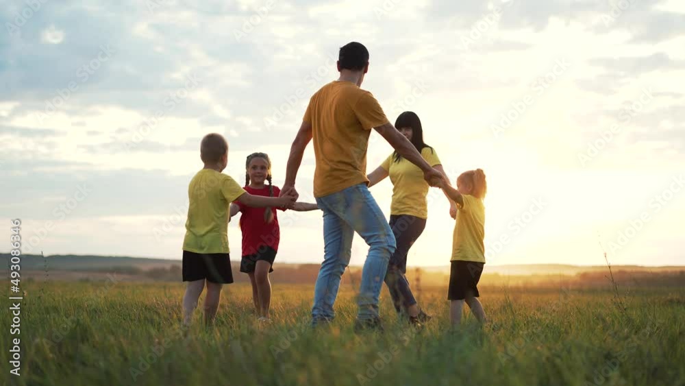 Happy family concept. Group of people hold hands in round dance. Children and parents are play in park on grass. Active lifestyle concept Family on green grass. Happy children play round dance in park Happy family concept. Group of people hold hands in round dance. Children and parents are play in park on grass. Active lifestyle concept Family on green grass. Happy children play round dance in park